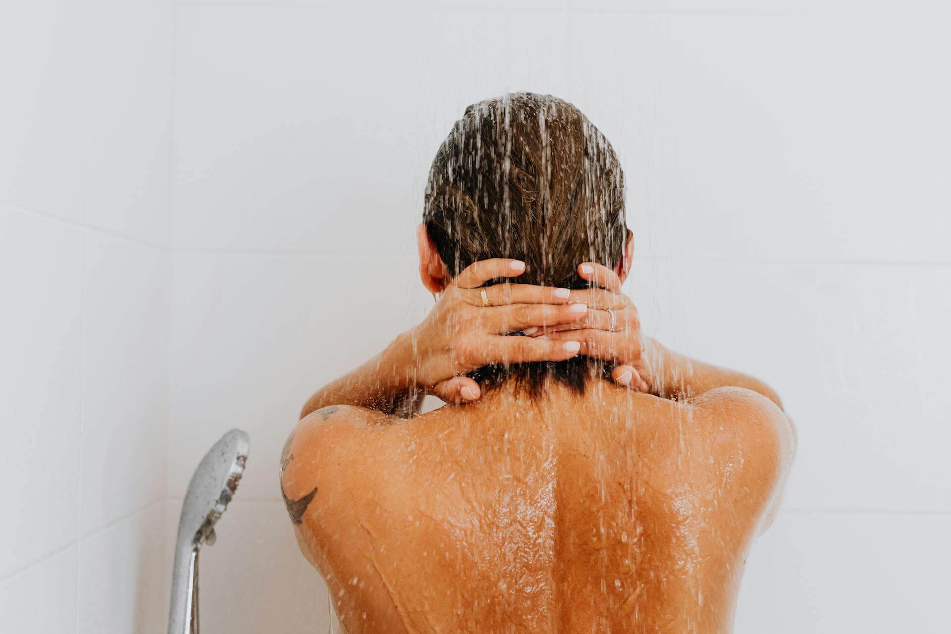 A woman with brown hair washes her hair in the shower as the water flows from the shower head