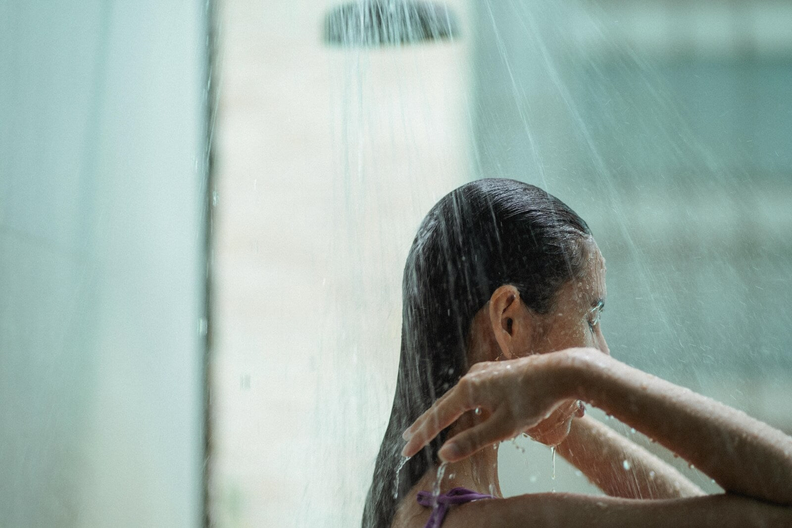 A woman takes a relaxing shower with a window looking out to the city in the background.